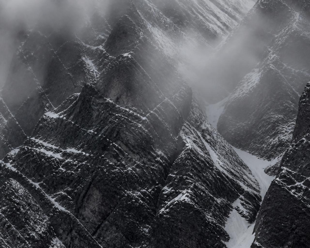 Tight crop of a steep rock face with snow in its crevices, partly obscured by fog
